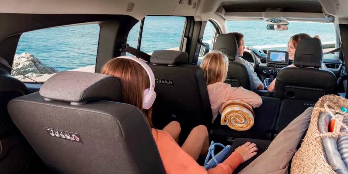 Familia viajando en coche el&eacute;ctrico hacia la playa, disfrutando del paisaje mar&iacute;timo y la comodidad del veh&iacute;culo.