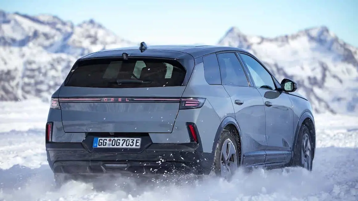 Coche el&eacute;ctrico Opel conduciendo en nieve en un paisaje monta&ntilde;oso invernal.