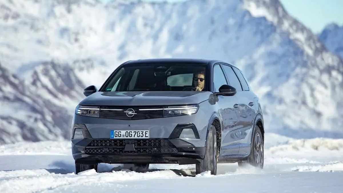 Autom&oacute;vil el&eacute;ctrico Opel conducido por carretera nevada con fondo de monta&ntilde;as. Proyecto de movilidad el&eacute;ctrica y ecol&oacute;gica.