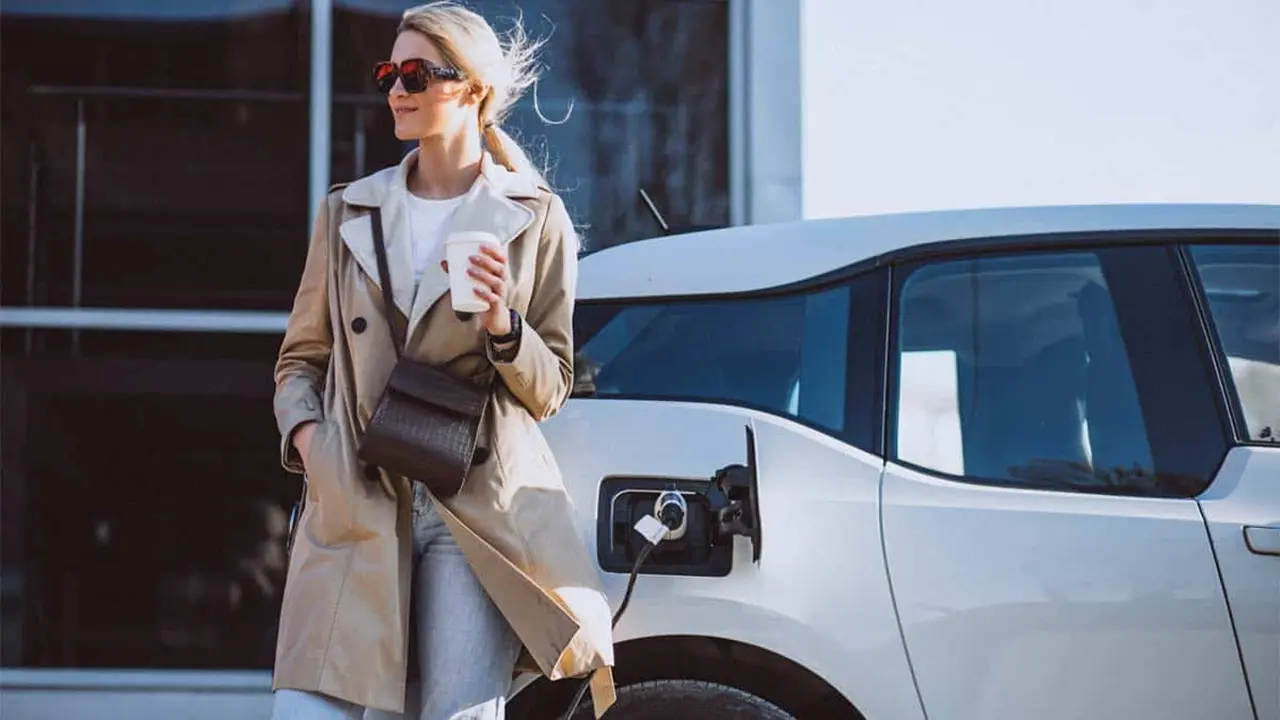 Persona cargando coche el&eacute;ctrico mientras toma un caf&eacute;