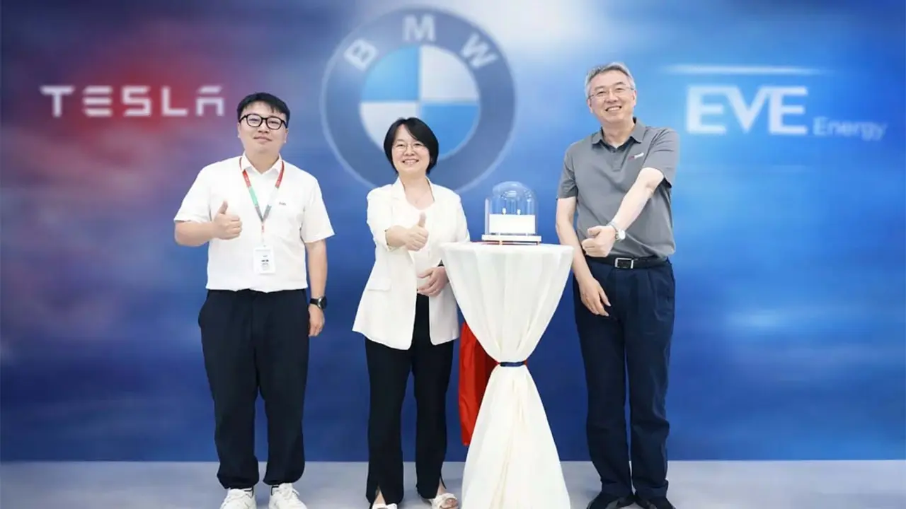 Tres profesionales en un evento de movilidad el&eacute;ctrica, celebrando con un pastel y mostrando entusiasmo por la innovaci&oacute;n en veh&iacute;culos el&eacute;ctricos.