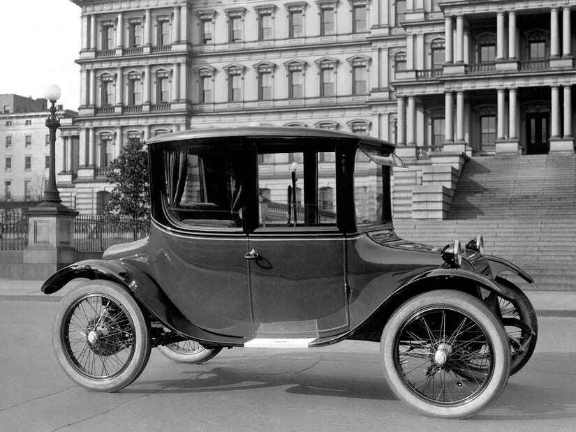 Coche eléctrico vintage en una calle urbana con edificio histórico de fondo.